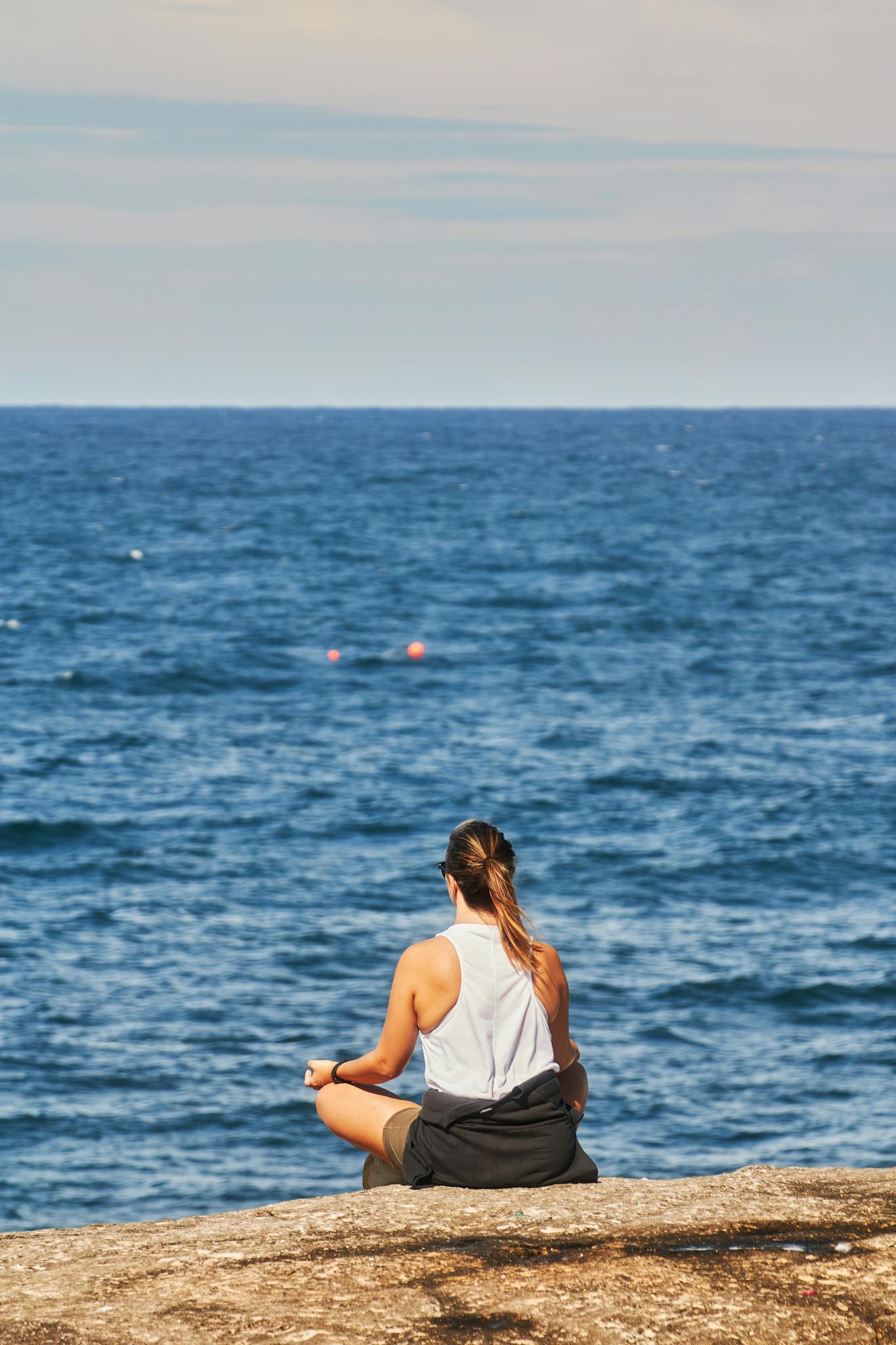 A woman meditating on a rock by the ocean